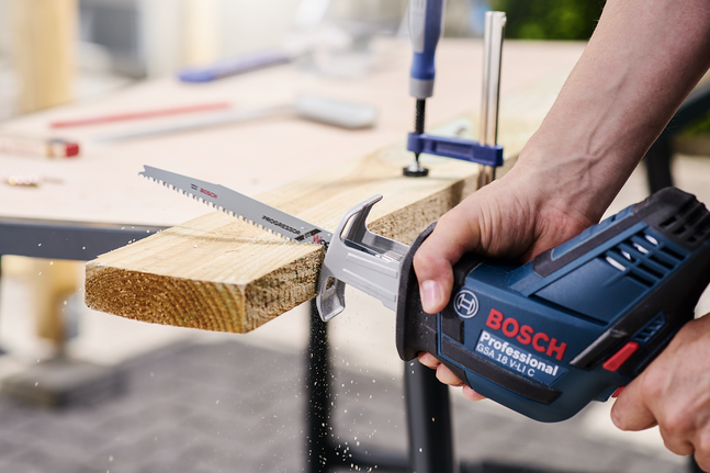 一個人在工作台上用往復鋸切割木板。