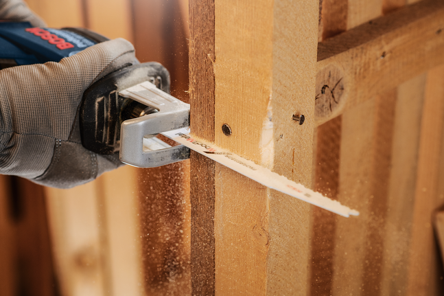 一名穿戴安全裝備的人員用往復鋸切割木樑。