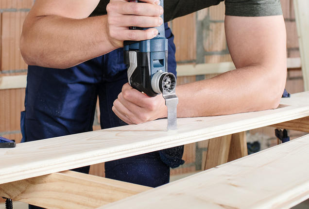 一名男子在建築工地使用電動工具切割木材。