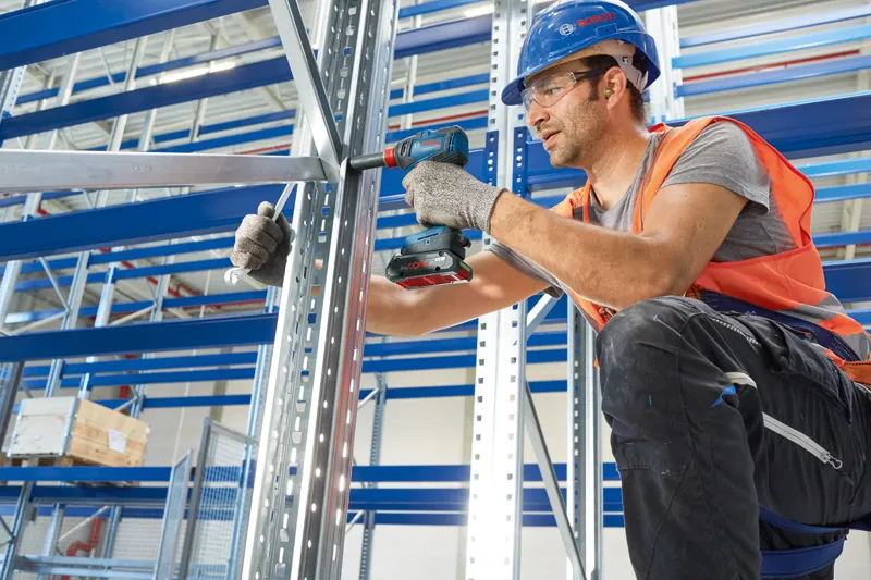 一名配戴安全設備的人員使用無線電鑽固定金屬框架。.