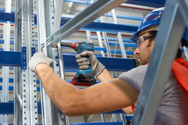 一名配戴安全設備的人員在金屬框架上使用無線電鑽。.