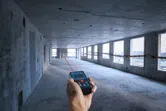 一名男子使用雷射測量儀測量未完工混凝土房間內的距離。.