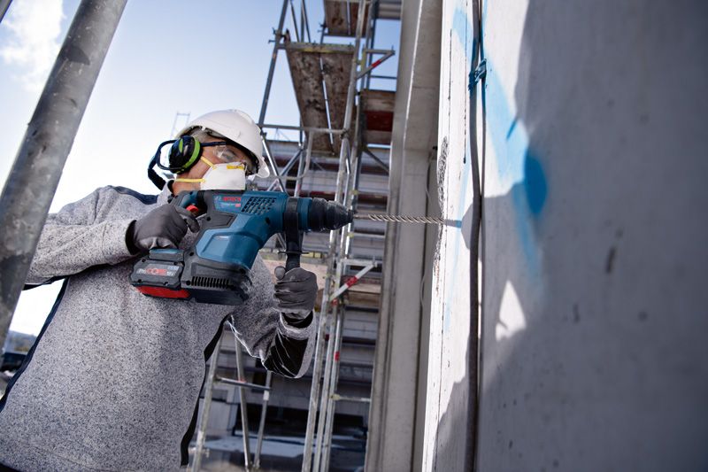 一名穿戴安全裝備的工人正在建築工地上鑽混凝土牆。