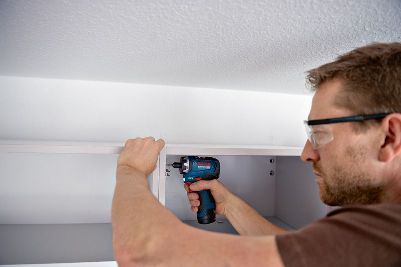 一名配戴安全設備的人員使用無線螺絲起子組裝櫥櫃。.