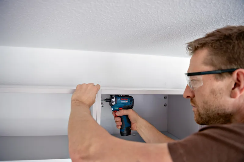 一名配戴安全設備的人員使用無線螺絲起子組裝櫥櫃。.