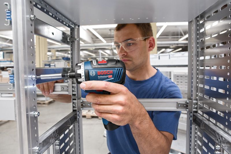 一名配戴安全設備的人員正在金屬框架上使用無線螺絲起子。.