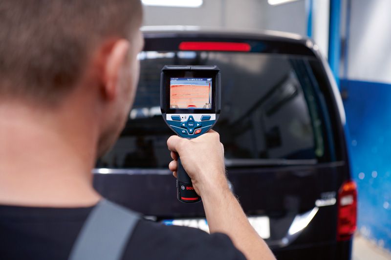 一個人使用熱像儀掃描車輛的後窗。.