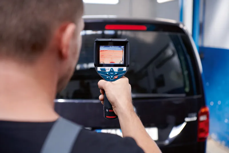 一名男子使用熱成像儀掃描黑色廂型車的後窗。