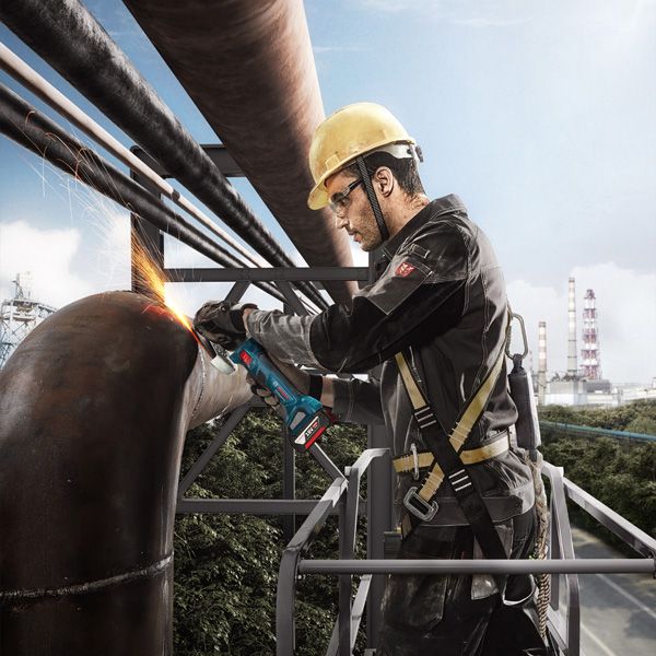 一名配戴安全設備的人員正在用角磨機打磨一根大型金屬管。.