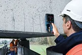 一名配戴安全設備的人員使用電子偵測器掃描混凝土梁。