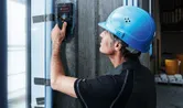 一名配戴安全設備的人員使用探測工具掃描混凝土牆。