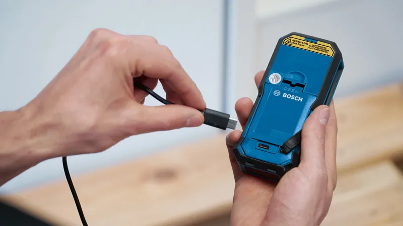 一個人將充電線連接到手持電動工具的背面。.