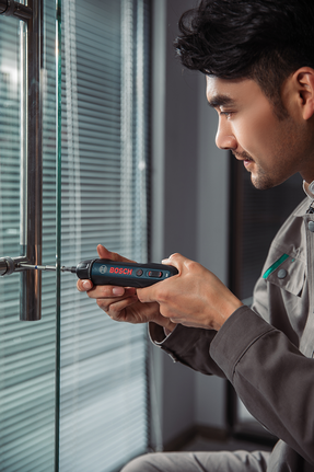 有人用無線螺絲起子將螺絲旋到玻璃門把手上。