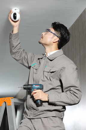 一名穿戴安全裝備的人員正在用電鑽安裝監視器。