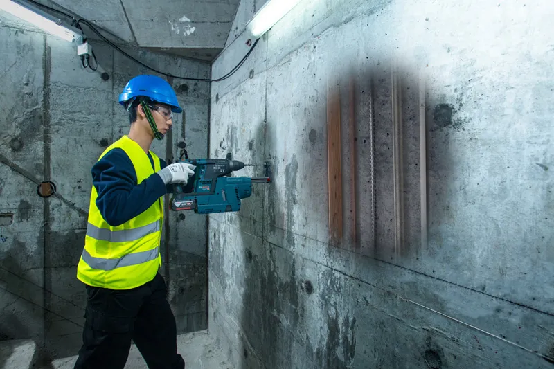 一名配戴安全設備的人員使用探測器掃描混凝土牆，露出裡面的管道。.