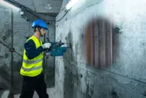 一名配戴安全設備的人員使用探測器掃描混凝土牆，露出裡面的管道。