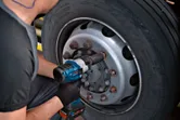 一名佩戴安全設備的人員使用衝擊扳手來擰緊卡車車輪上的螺栓。.