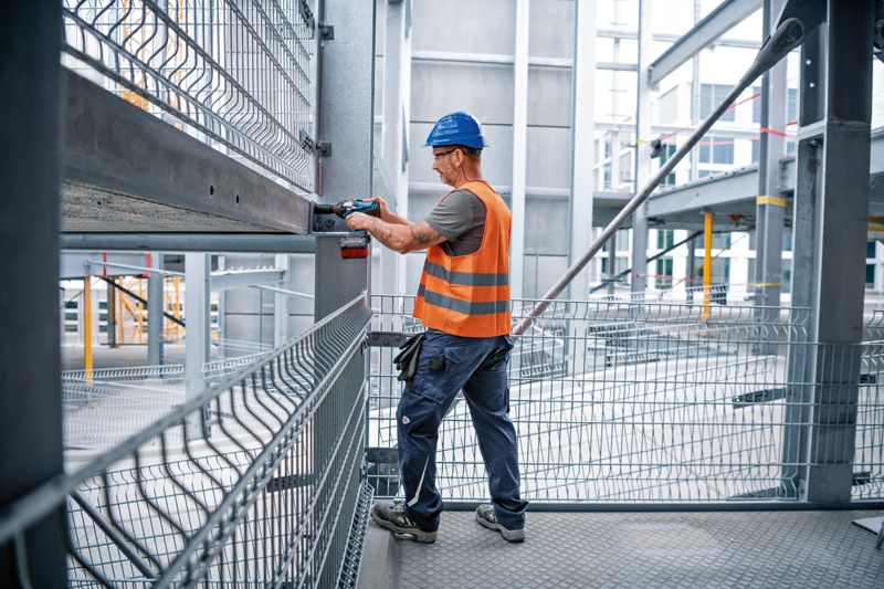 施工現場，一名配戴安全設備的人員使用衝擊扳手來擰緊鋼樑。.