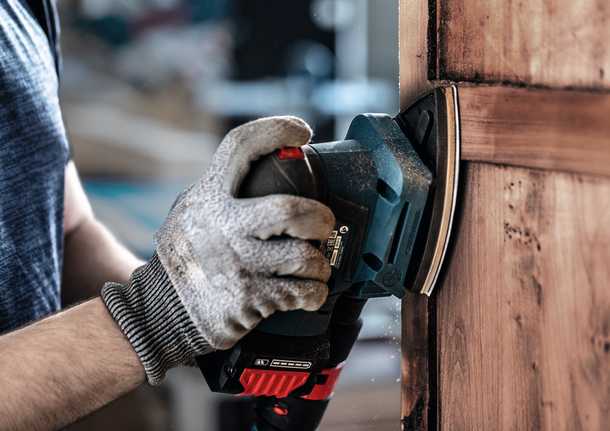 配戴安全設備的人員使用電動工具打磨木門。