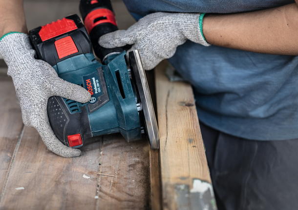 配戴安全設備的人員使用電動工具打磨木質表面。