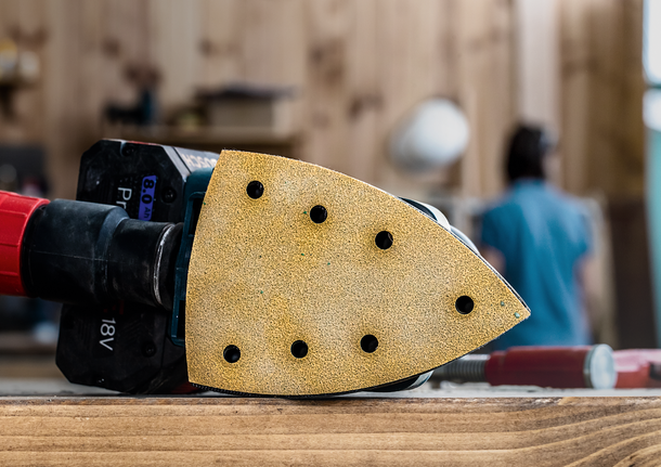 細節砂光機放置在車間的木質表面上，背景中有一個人物。