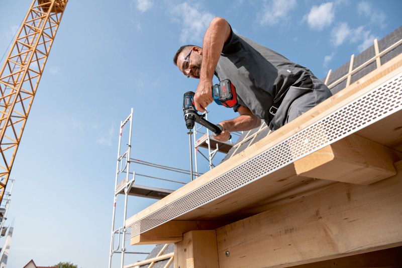 一名佩戴安全設備的人員正在向正在建造的建築物的木樑上鑽孔。.