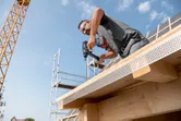 一名佩戴安全設備的人員正在向正在建造的建築物的木樑上鑽孔。
