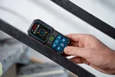 一個人拿著雷射測距儀靠在金屬欄桿上。