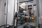 一名佩戴安全設備的人員使用無線熱風槍對電線進行加熱。