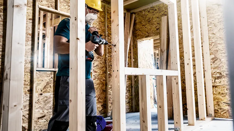 一名配戴安全設備的人員在建築工地上鑽木框架。