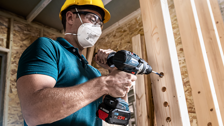 配戴安全設備的人員在木樑上鑽孔。