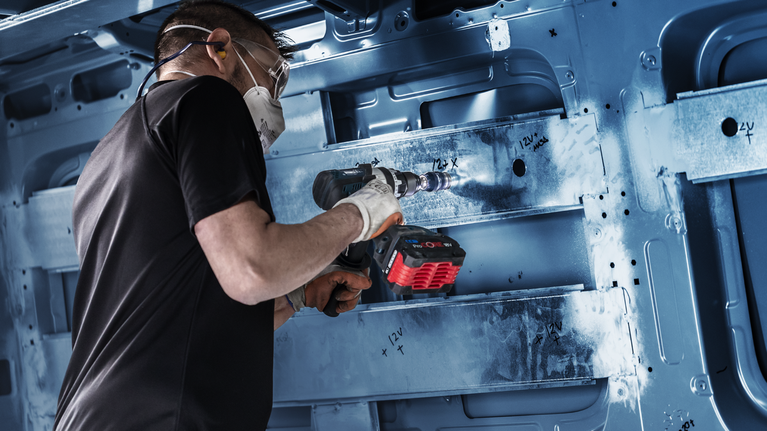 一名身穿安全裝備的人員正在車內鑽孔，鑽穿金屬框架。