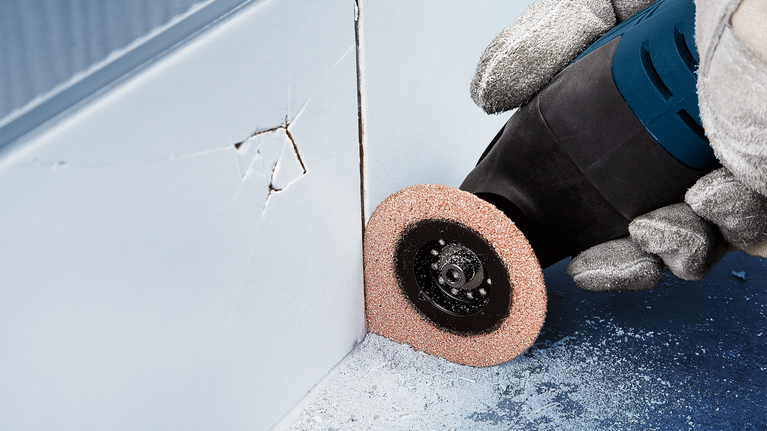 配戴安全設備的人員使用旋轉工具在牆角附近進行打磨。