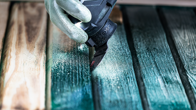 配戴安全設備的人員使用電動工具打磨木板上的油漆。