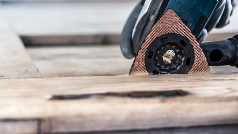 配戴安全設備的人用多功能工具打磨木材。