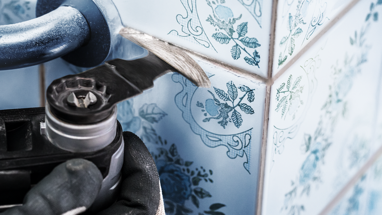 超耐久鑽石弧形刀專業款 MATI 68 RD4,68 x 30 mm 一名配戴安全設備的人員使用電動工具去除牆磚之間的水泥漿。