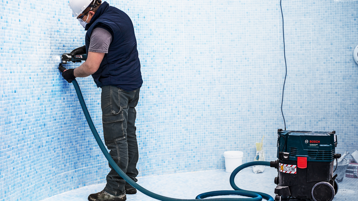 一名身穿安全裝備的人員在空泳池中鑽入磁磚牆。