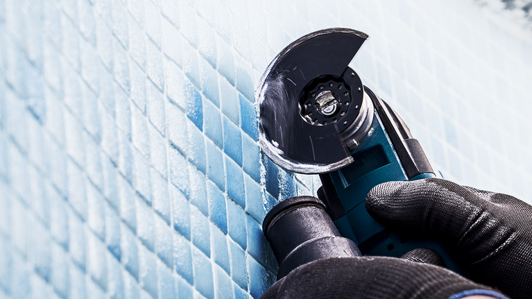 配戴安全設備的人員使用角磨機切割藍色磁磚。