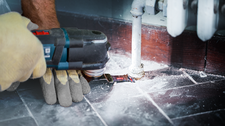 一名配戴安全設備的人員使用電動工具切割管道周圍的地板。