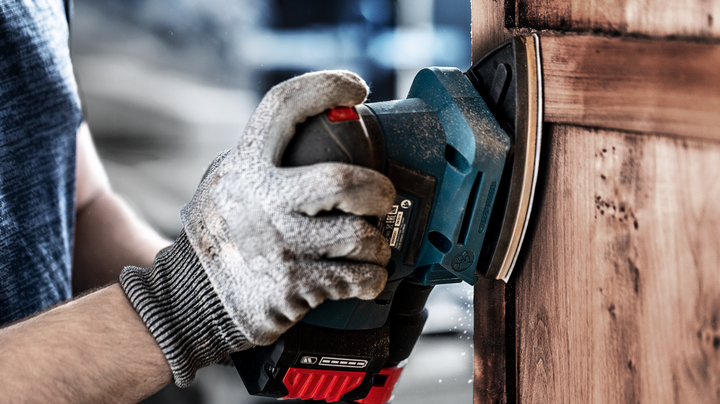 一名配戴安全設備的人員正在用電動砂光機打磨木門。