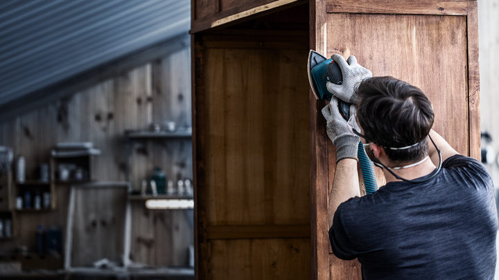 配戴安全設備的人員使用電動工具打磨木製櫥櫃。