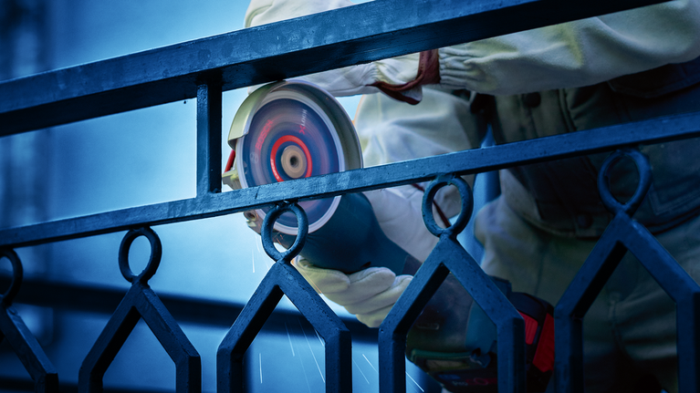 超耐久鑽石金屬切片專業款大尺寸 355 x 25.4 mm 一名佩戴安全設備的人正在用電動工具磨金屬柵欄。