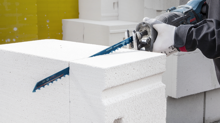 配戴安全設備的人員用往復鋸切割白色混凝土塊。