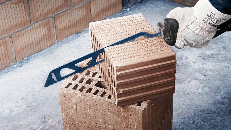 配戴安全設備的人員用手鋸切割磚塊。