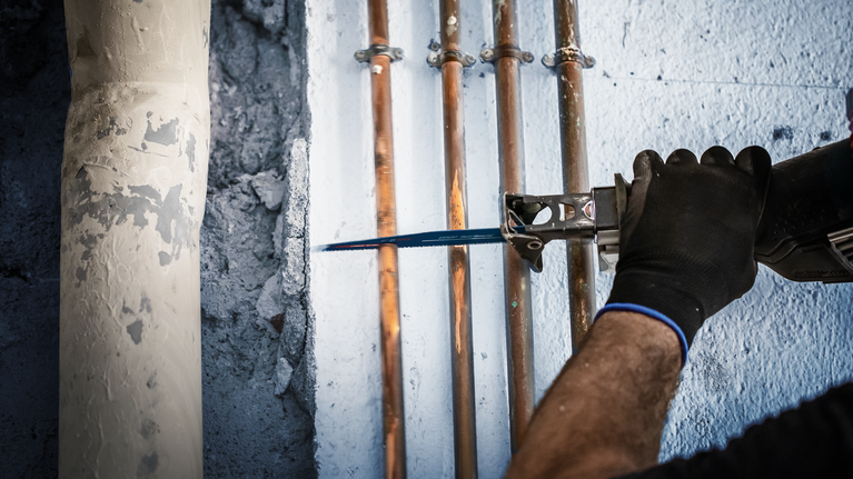 一個人用往復鋸切割安裝在牆上的銅管。