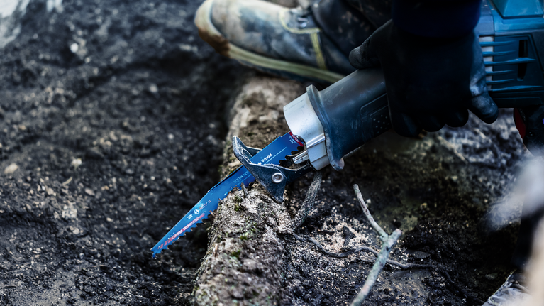 EXPERT ‘Tough Wood’ S 1142 KHM 軍刀鋸 1 件式 配戴安全設備的人員使用往復鋸切斷樹根。