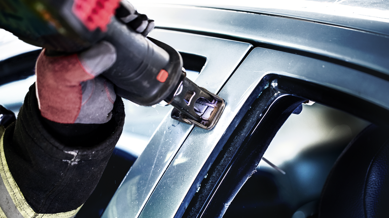 一名配戴安全設備的人員使用電動工具切割汽車窗框。