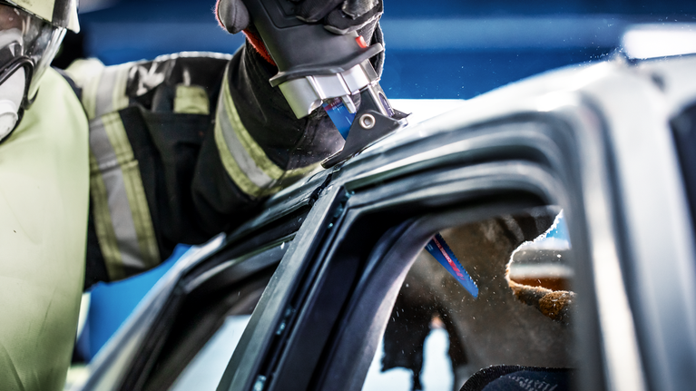 一名配戴安全設備的人使用往復鋸切割汽車車頂。