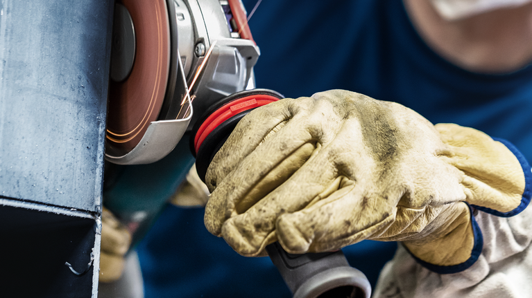 配戴安全設備的人員使用旋轉角磨機拋光金屬。