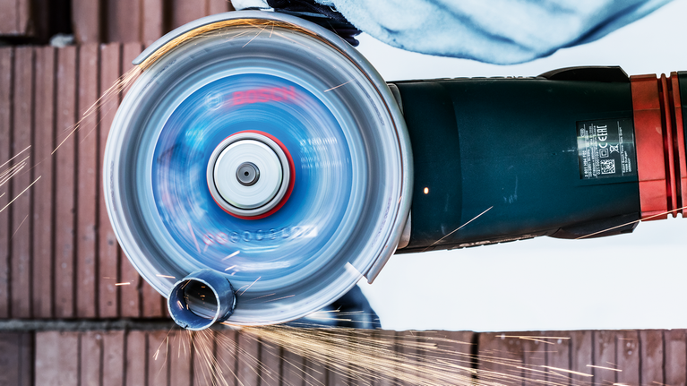 一名配戴安全設備的人員正在使用旋轉角磨機切割金屬管路。